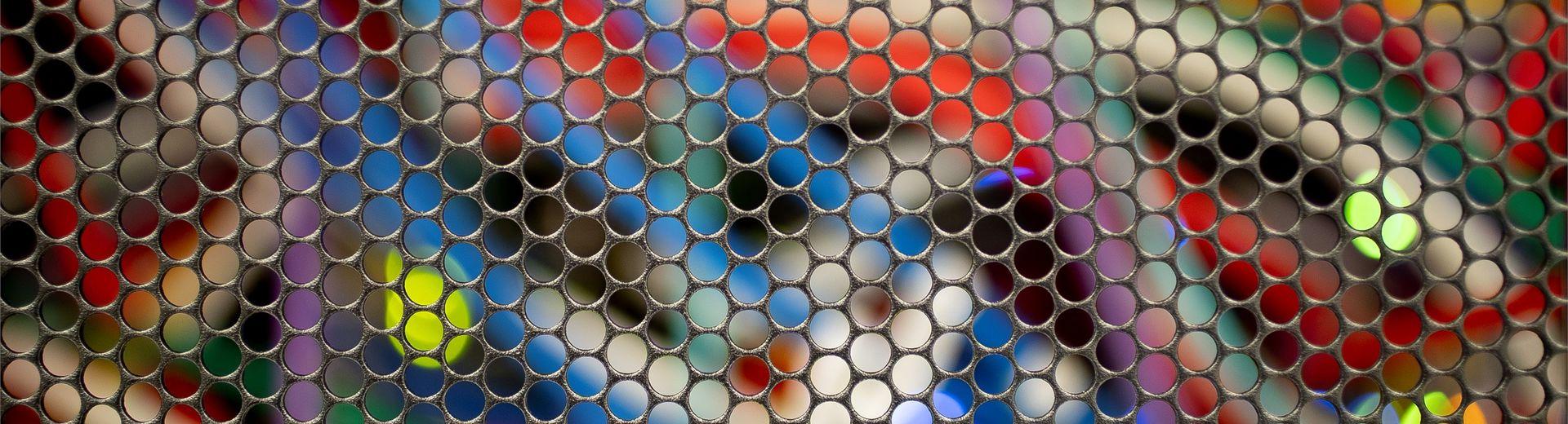 Close up picture of colorful computer cables behind a metal grid of circles.